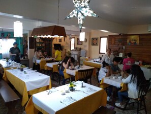 Un restaurante con mesas dispuestas para comer, una lámpara decorativa grande en el techo y una pared de madera con obras de arte.