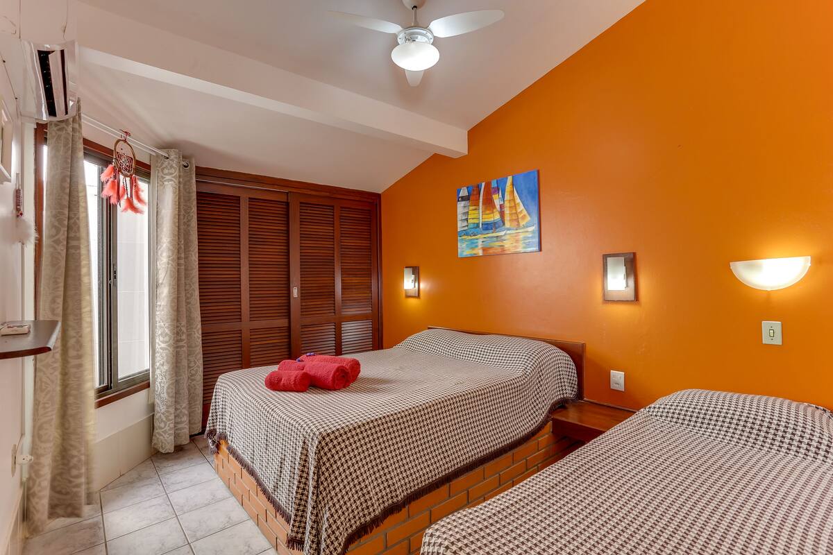 A hotel room with two beds, a ceiling fan, a painting of a sailboat, and a window with curtains.