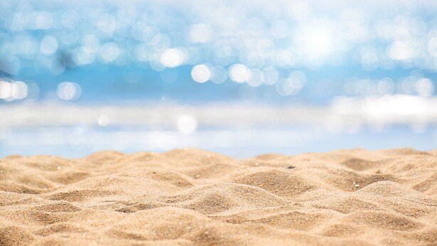 Ein Sandstrand mit unscharfem Hintergrund aus Meer und Himmel.