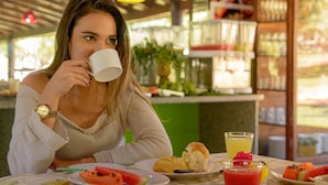 Une personne assise à une table devant une assiette de nourriture, une boisson et une tasse.
