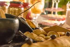 A close-up of a buffet table with various food items, including rolls and a metal bowl.