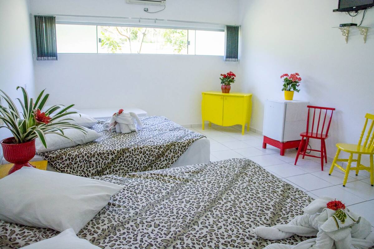 Una habitación de hotel con dos camas, un armario amarillo, una silla roja y una planta en maceta.