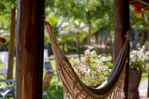 Una hamaca atada entre dos postes de madera en un jardín con plantas en macetas y follaje al fondo.