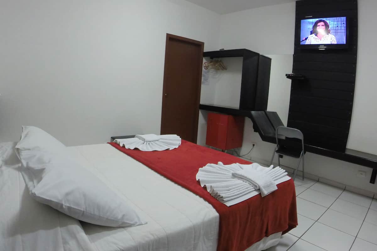 Ein Hotelzimmer mit einem Bett, einer roten Tagesdecke, weißen Kissen, einem an der Wand befestigten Fernseher, einem Schreibtisch und einem Stuhl.