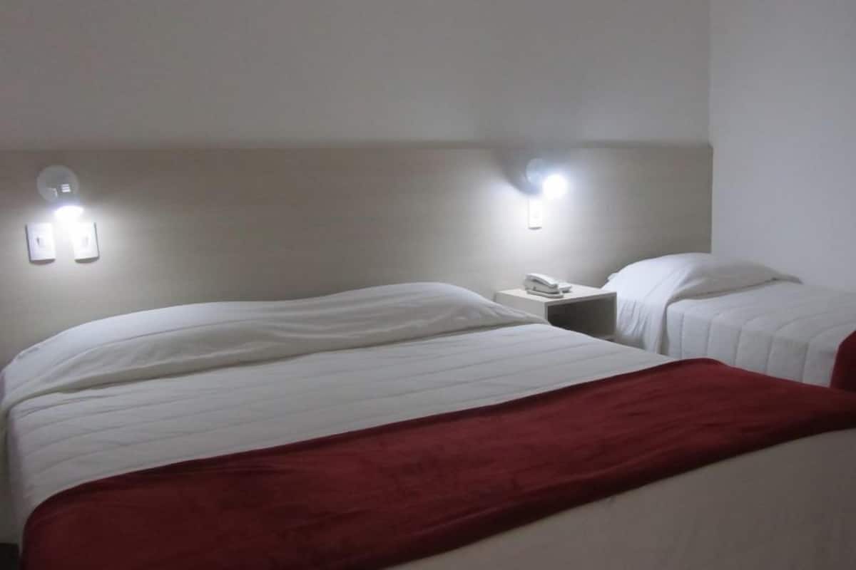 Ein Hotelzimmer mit zwei Betten, jeweils mit weißer Bettwäsche und einer roten Decke. Zwei Nachttische mit Lampen und einem Telefon sind vorhanden.