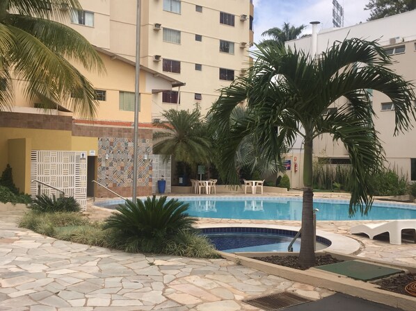 A swimming pool area with a tiled deck, palm trees, and a building with multiple windows in the background. - Hotel Morada das Aguas (Caldas Novas)