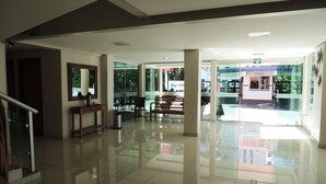 Un lobby amplio con suelo de baldosas pulidas, una mesa de recepción y un área de descanso con sillas y un banco.