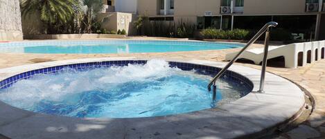 A swimming pool with a hot tub in the foreground, surrounded by stone tiles and a palm tree.