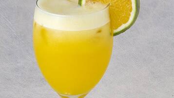 Un vaso de bebida amarilla con una rodaja de lima y una pajita.