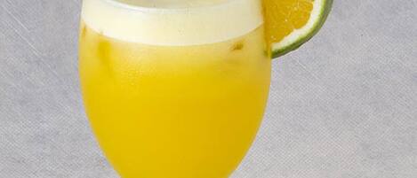 A glass of yellow beverage with a lime slice and a straw.