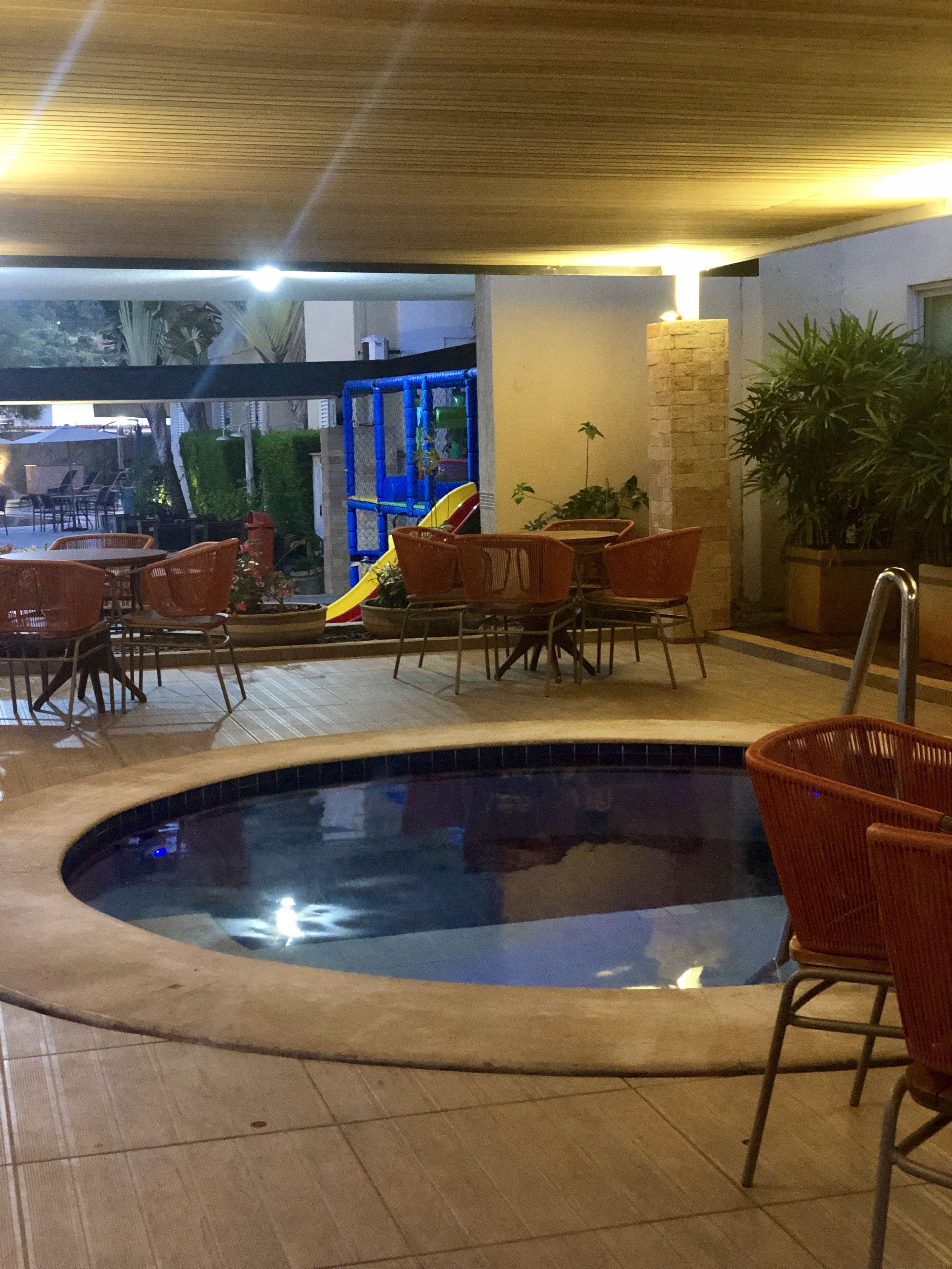 Zona de piscina interior con tobogán, sillas de mimbre y pared de piedra.