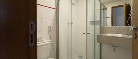 A bathroom with a glass-enclosed shower, a toilet, and a sink with a mirror above it.