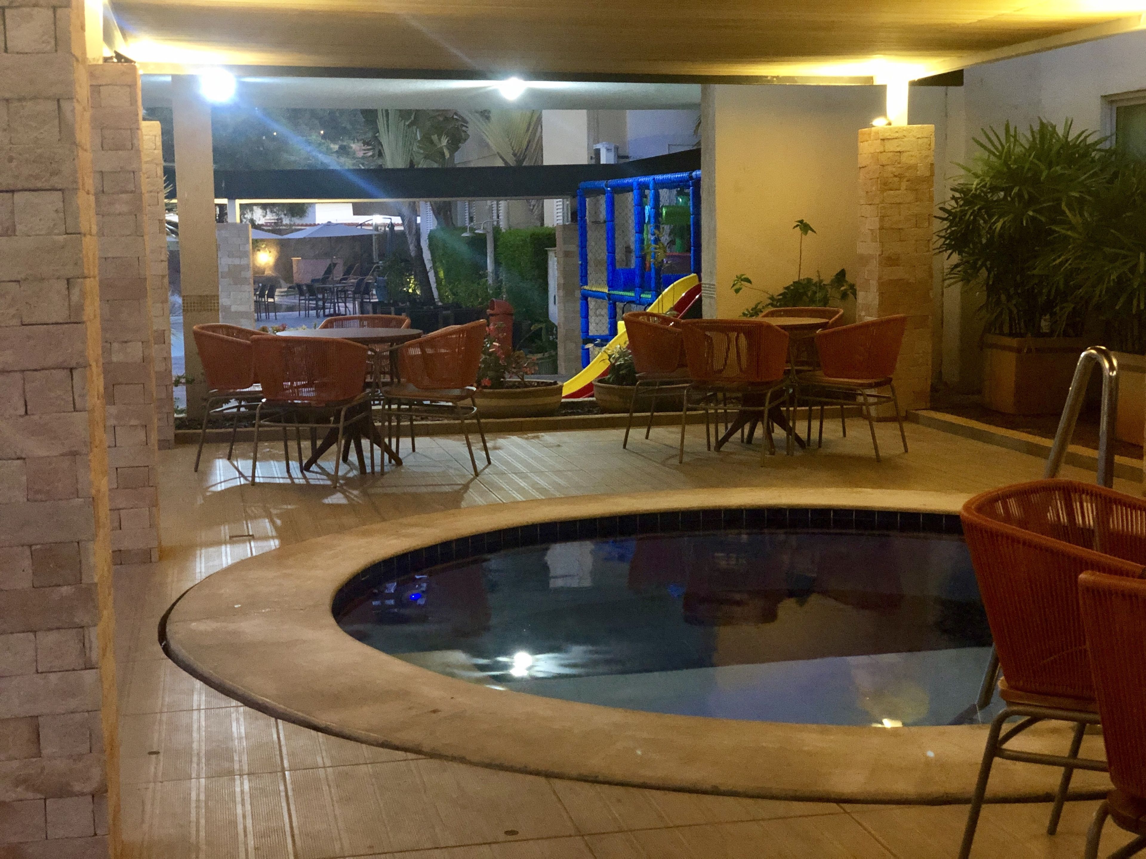 An indoor swimming pool area with tiled flooring, surrounded by wicker chairs and tables.