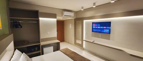 Ein Hotelzimmer mit Bett, Kleiderschrank, Schreibtisch und einem an der Wand befestigten Fernseher.
