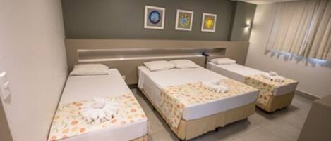 Habitación de hotel con tres camas, un ventanal con cortinas y una pared con tres cuadros enmarcados.