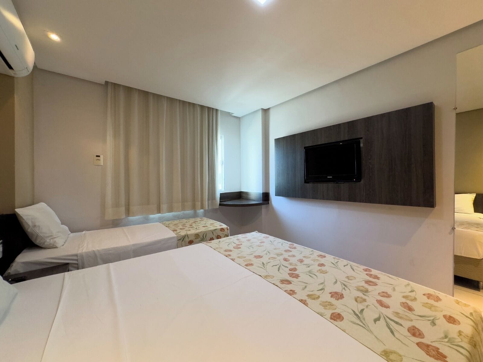 Habitación de hotel con dos camas, un televisor montado en la pared y una ventana con cortinas.