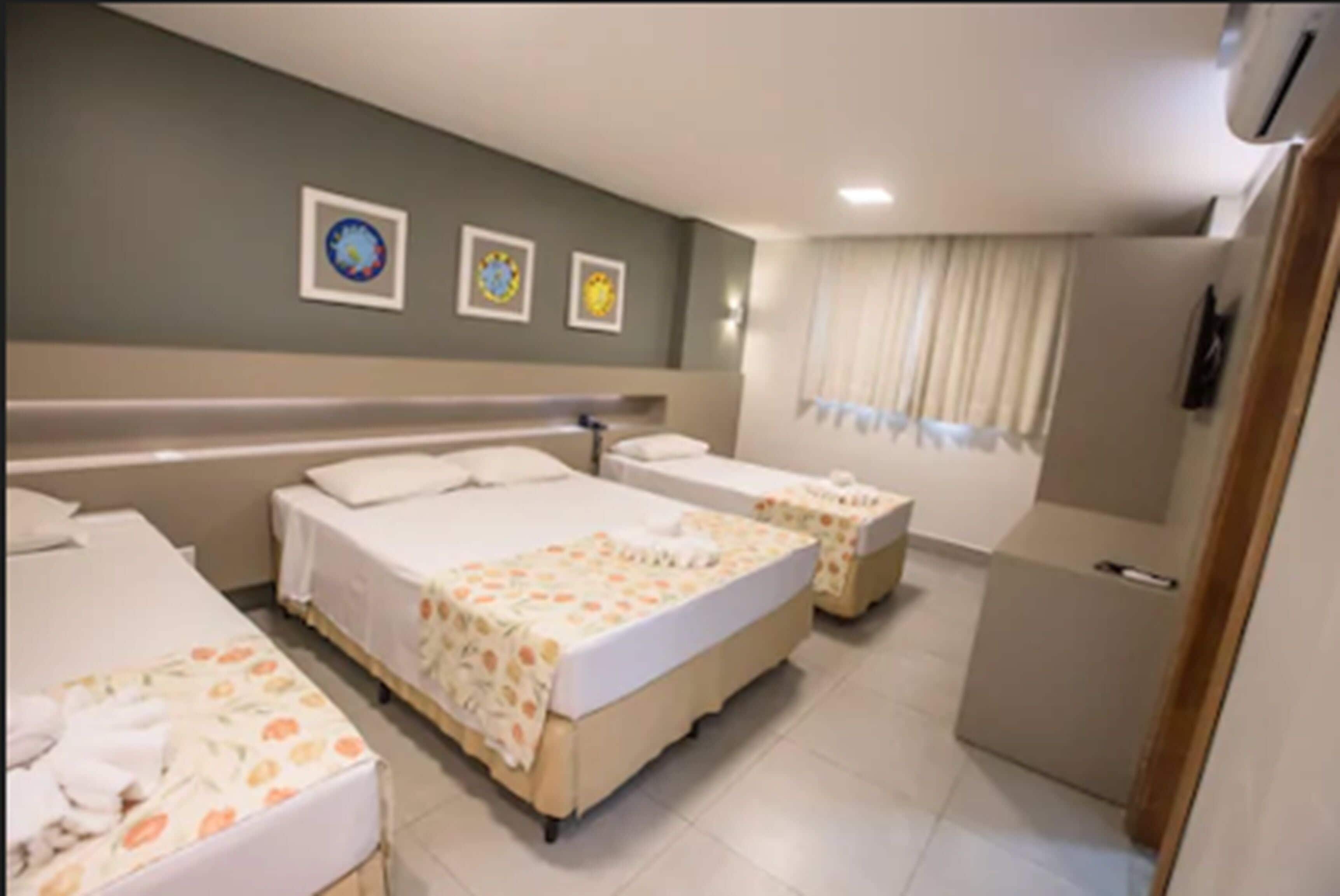 A hotel room with two beds, a small desk, and a window with curtains.