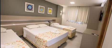A hotel room with two beds, a small desk, and a window with curtains.