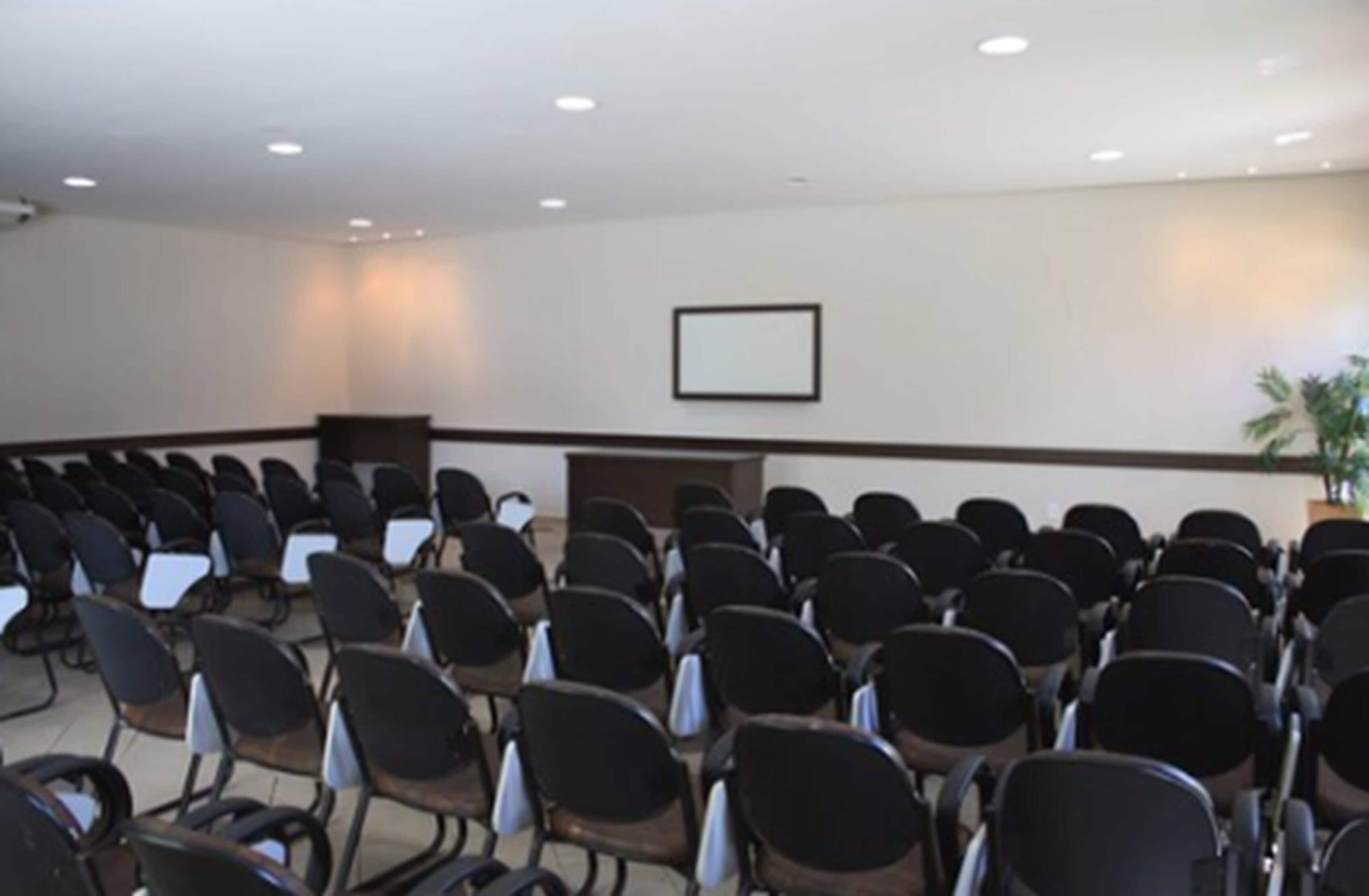 A conference room with rows of chairs, a podium, and a framed picture on the wall.