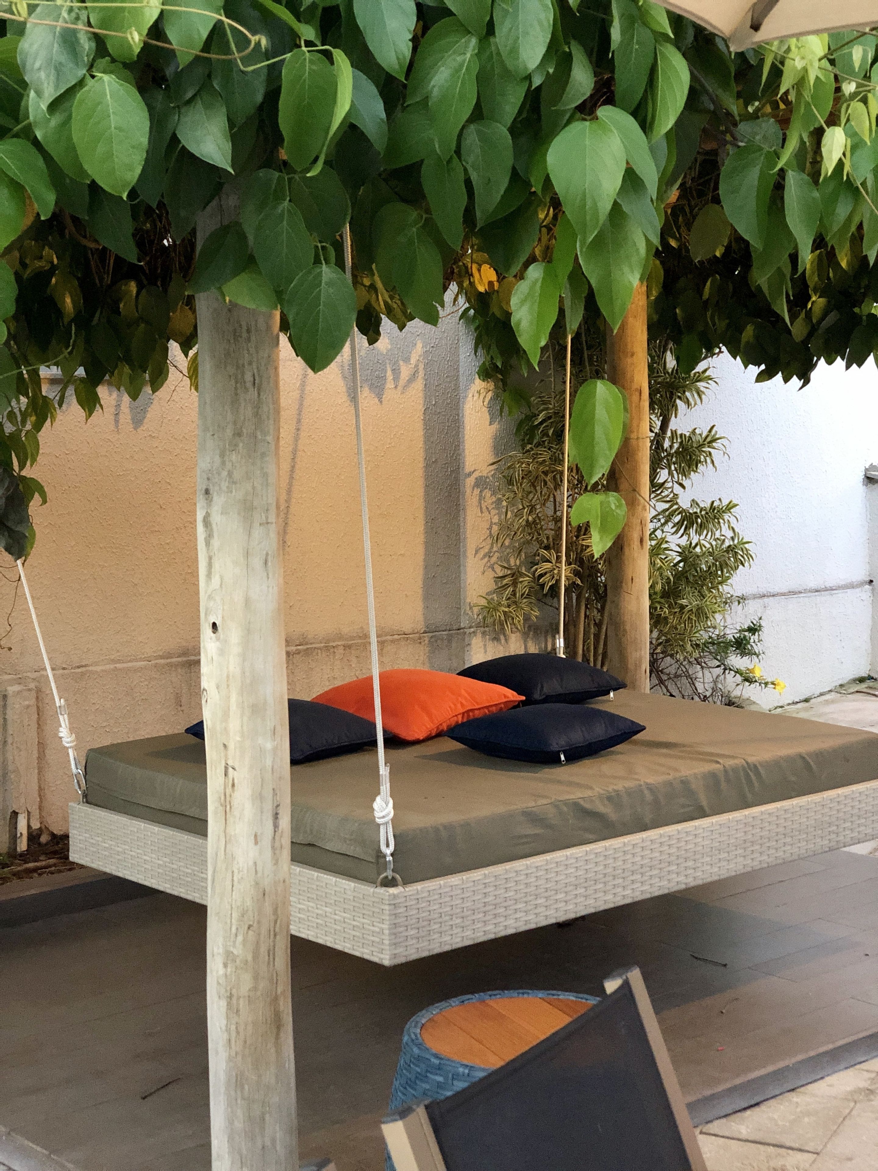 Un lit-hamac donnant sur un jardin, avec un mur blanc et un poteau en bois.