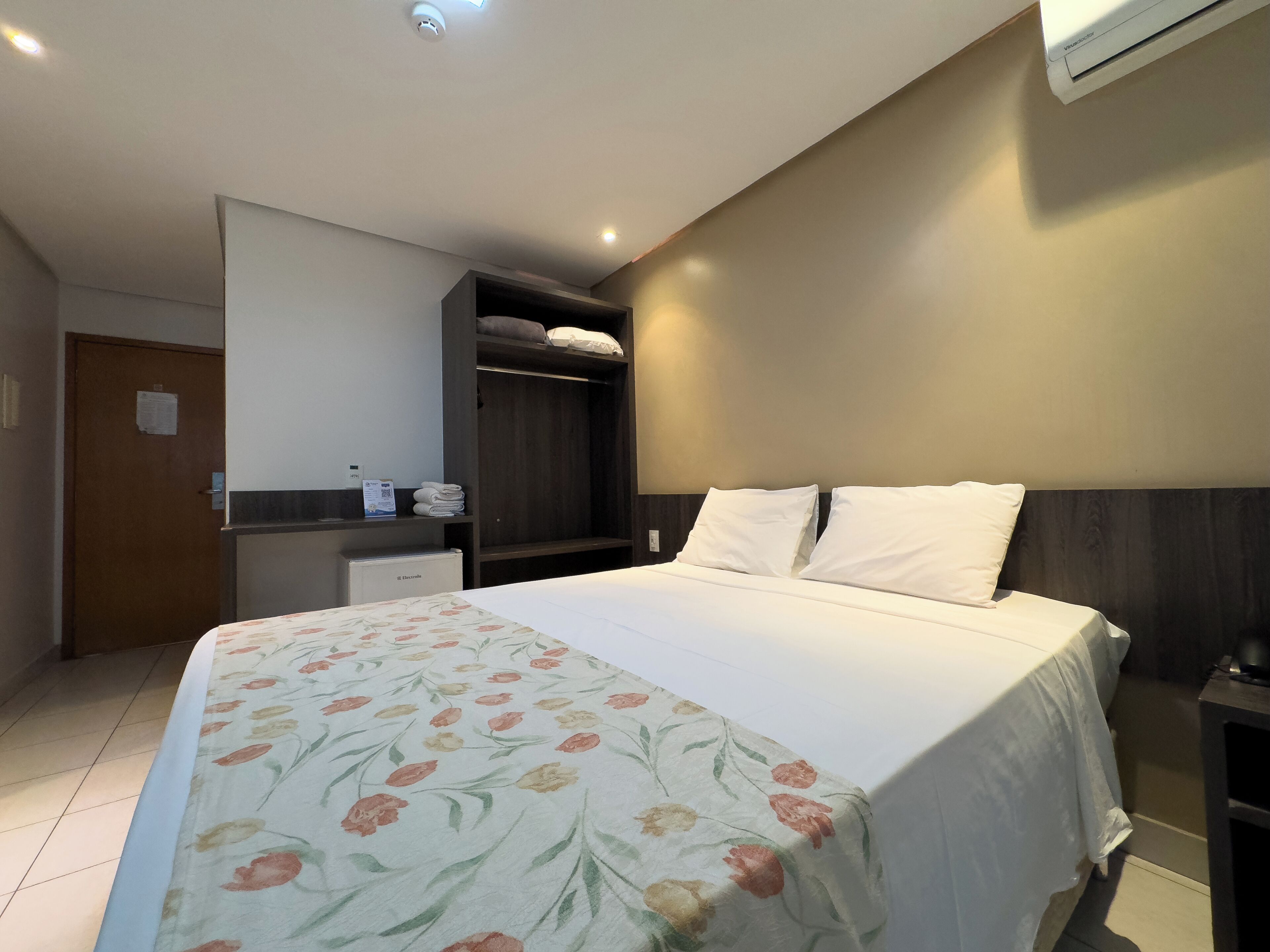 Habitación de hotel con cama, armario, escritorio y aire acondicionado.