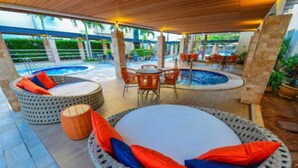 An outdoor seating area with wicker chairs and cushions, a pool, and a covered patio. - Hotel Morada do Sol (Caldas Novas)