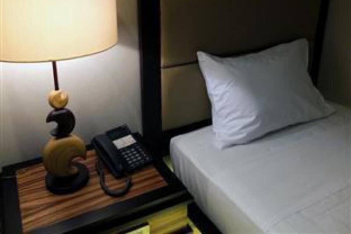Quarto de hotel com cama, mesa de cabeceira, luminária e telefone.
