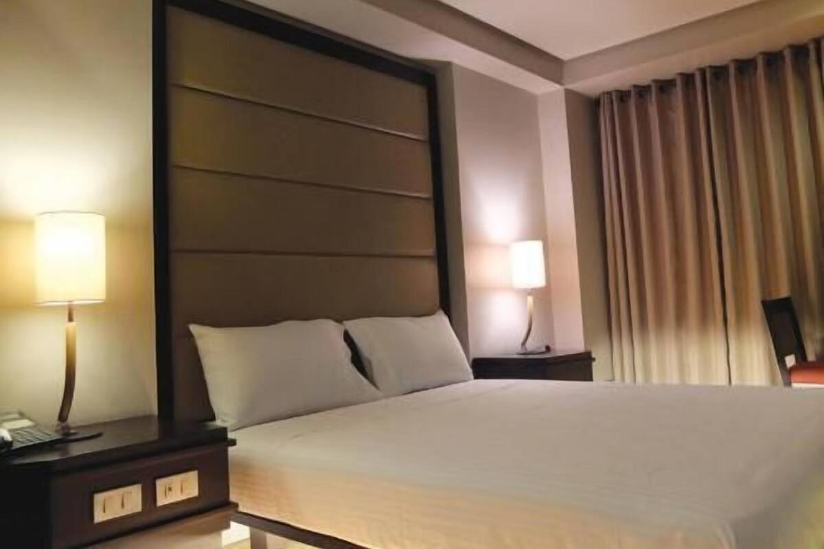Quarto de hotel com uma cama grande, duas mesas de cabeceira e um painel de cabeceira.