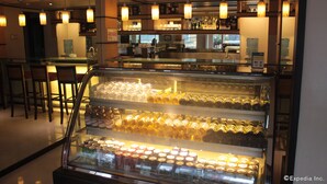Una zona de bar con un expositor de vidrio que contiene botellas y latas. Se ven sillas y mesas en primer plano, y una barra con un menú al fondo.