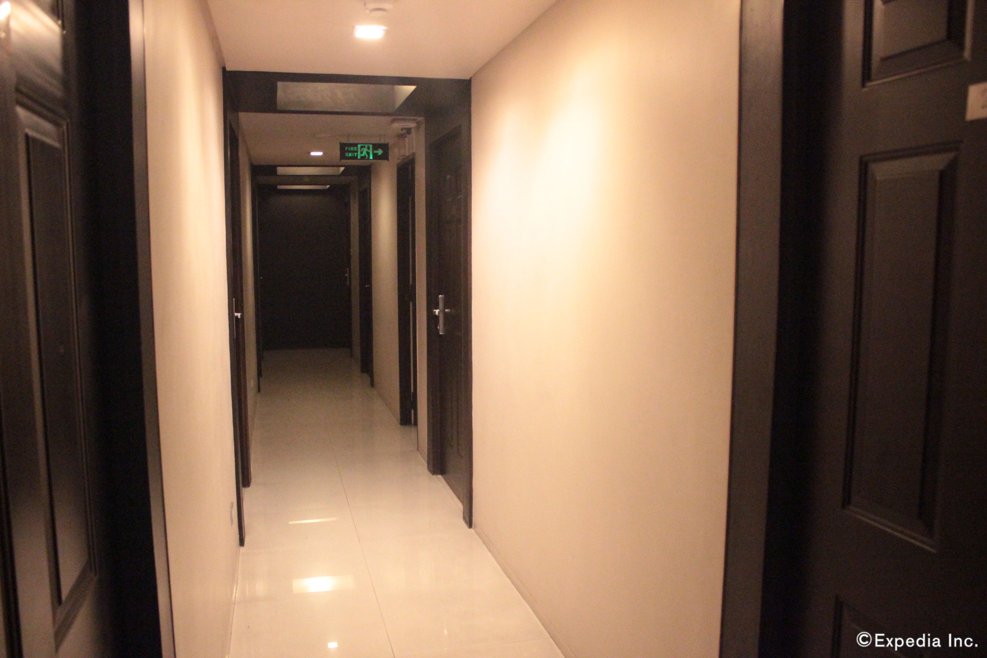 A hotel hallway with doors on both sides, a tiled floor, and an exit sign.