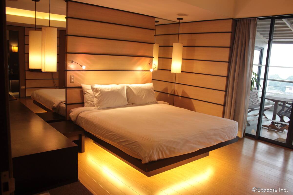 Quarto de hotel moderno com uma cama grande, luminárias laterais e vista para o exterior.