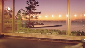 A room with a large window overlooking a body of water and a sunset. - Hotel Mikawa Kaiyoukaku (Gamagori)