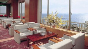 A hotel lobby with seating, a coffee table, and a large window with a view of the sea. - Hotel Mikawa Kaiyoukaku (Gamagori)