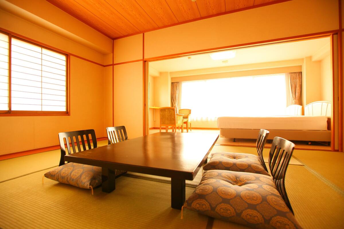 A tatami room with a low table, four chairs, a sofa, and a large window with curtains.