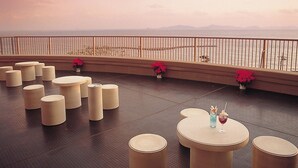 A terrace with round tables and chairs, a railing, and a view of the sea and mountains. - Hotel Mikawa Kaiyoukaku (Gamagori)