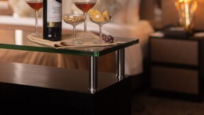 A hotel room with a glass coffee table, a bottle of wine, two wine glasses, and a small plate with snacks. - New World Suites (Bintulu)