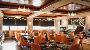 A dining area with round tables, orange upholstered chairs, and pendant lighting. - New World Suites (Bintulu)