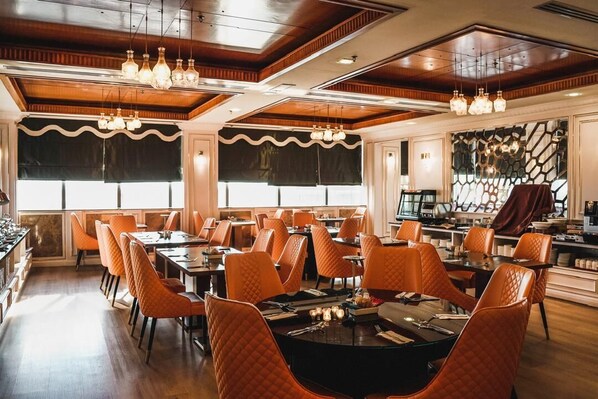 Comedor con mesas redondas, sillas tapizadas en naranja e iluminación colgante.