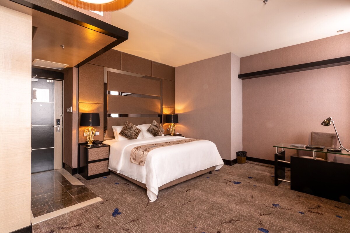 A modern hotel room with a large bed, a desk, and a separate seating area.