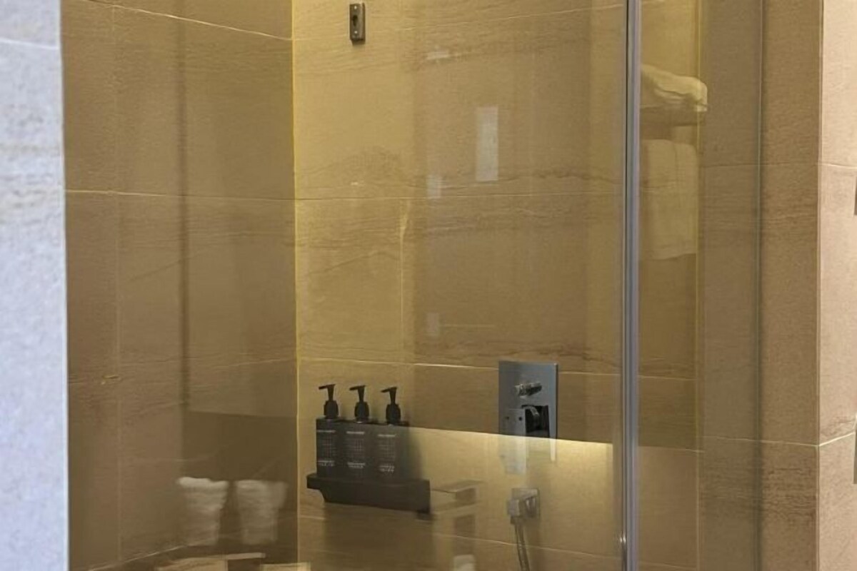 A glass-enclosed shower area with a hand dryer and toiletries.