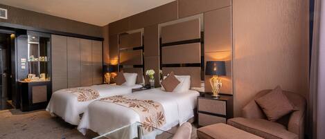 A hotel room with two beds, a sofa, a glass table, and a small desk with a lamp.