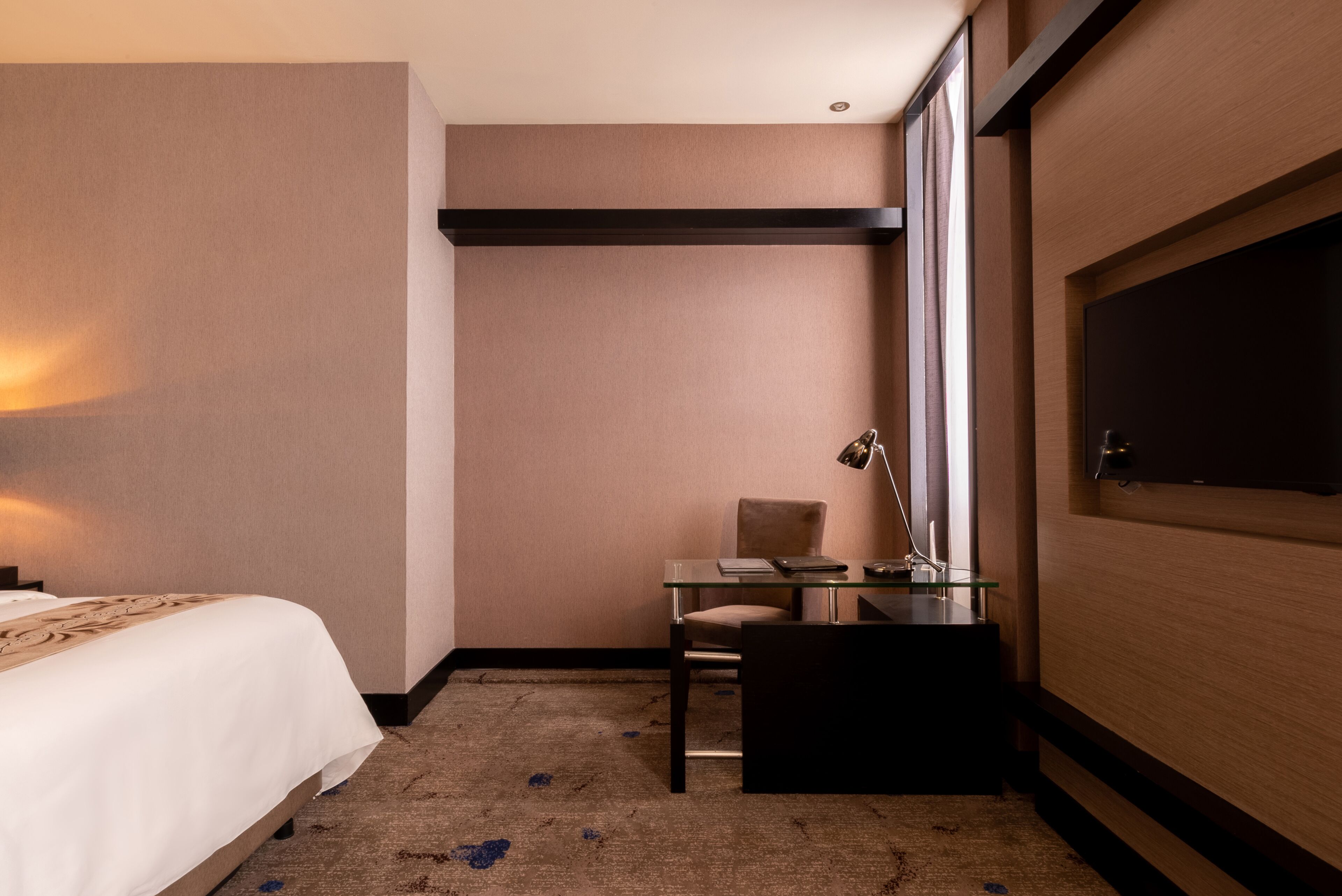 Une chambre d’hôtel avec un lit, un bureau et une chaise, une lampe et une grande fenêtre.