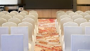 A conference room with rows of white chairs, a large screen, and a carpeted floor. - New World Suites (Bintulu)