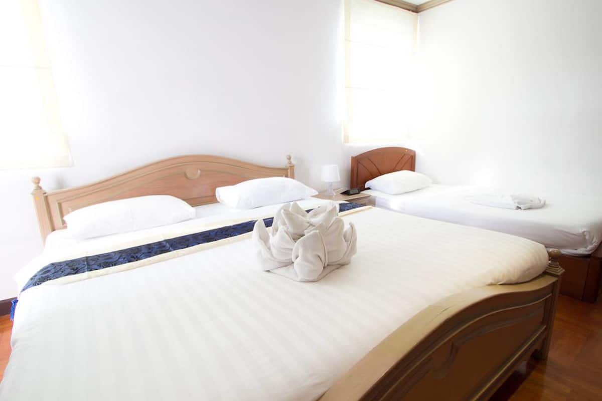 A hotel room with two beds, a wooden headboard, white bedding, and a towel arrangement on the bed.