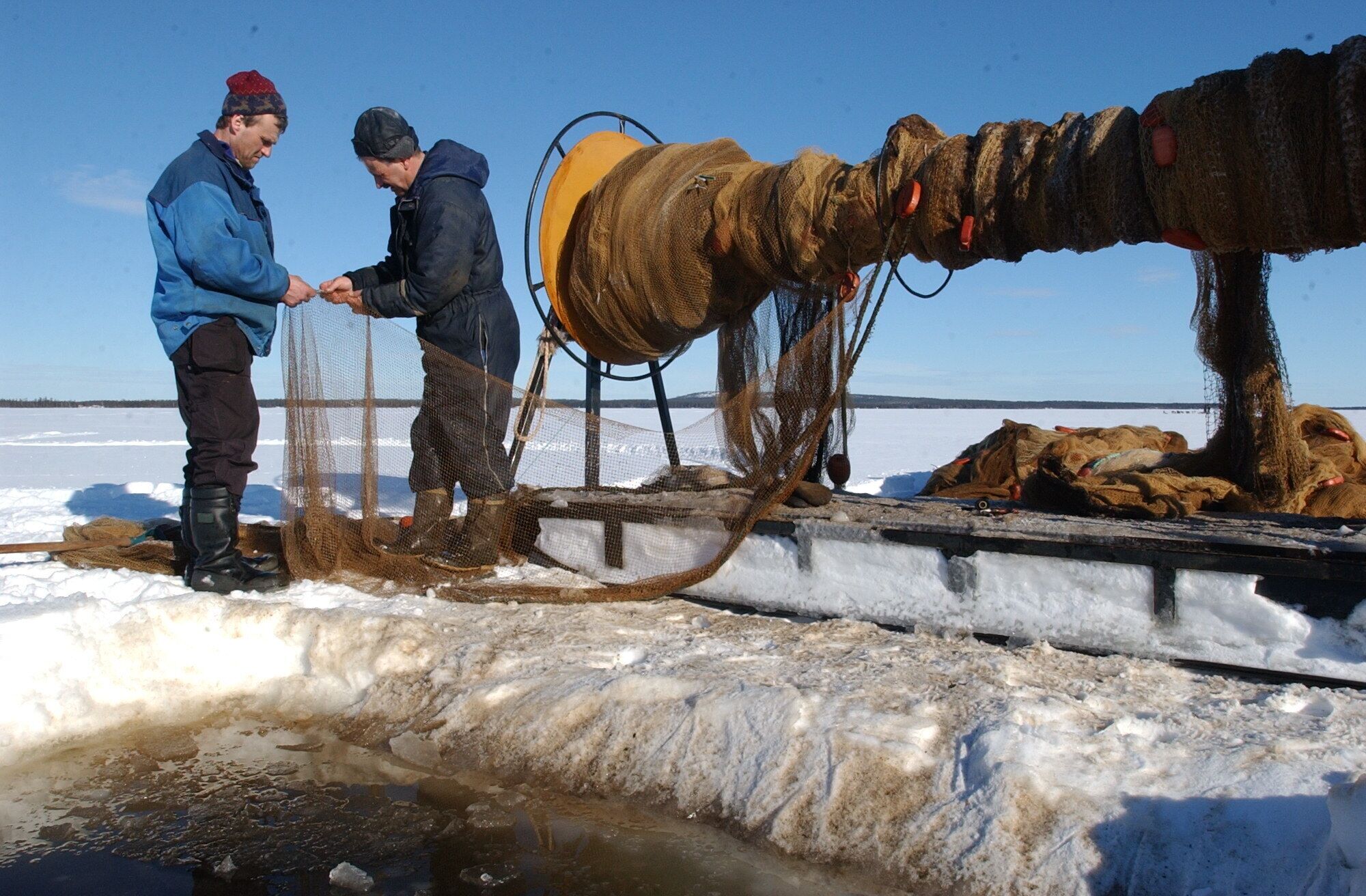 Two people standing on a dock, handling fishing nets and equipment.