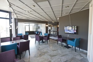 Un comedor moderno con suelo de mármol, sillas moradas y azules, y un televisor de pantalla plana montado en la pared.
