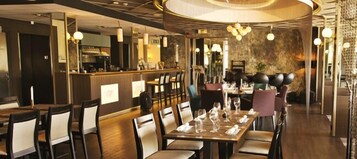 Un restaurante con área de bar, mesas dispuestas para comer y una pared de piedra al fondo.