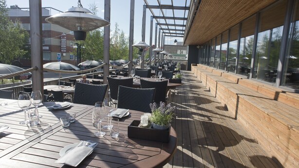 Un área de comedor al aire libre con mesas y sillas de madera, y sombrillas.
