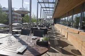 An outdoor dining area with wooden tables, chairs, and umbrellas. - Hotell Valhall (Kalix)
