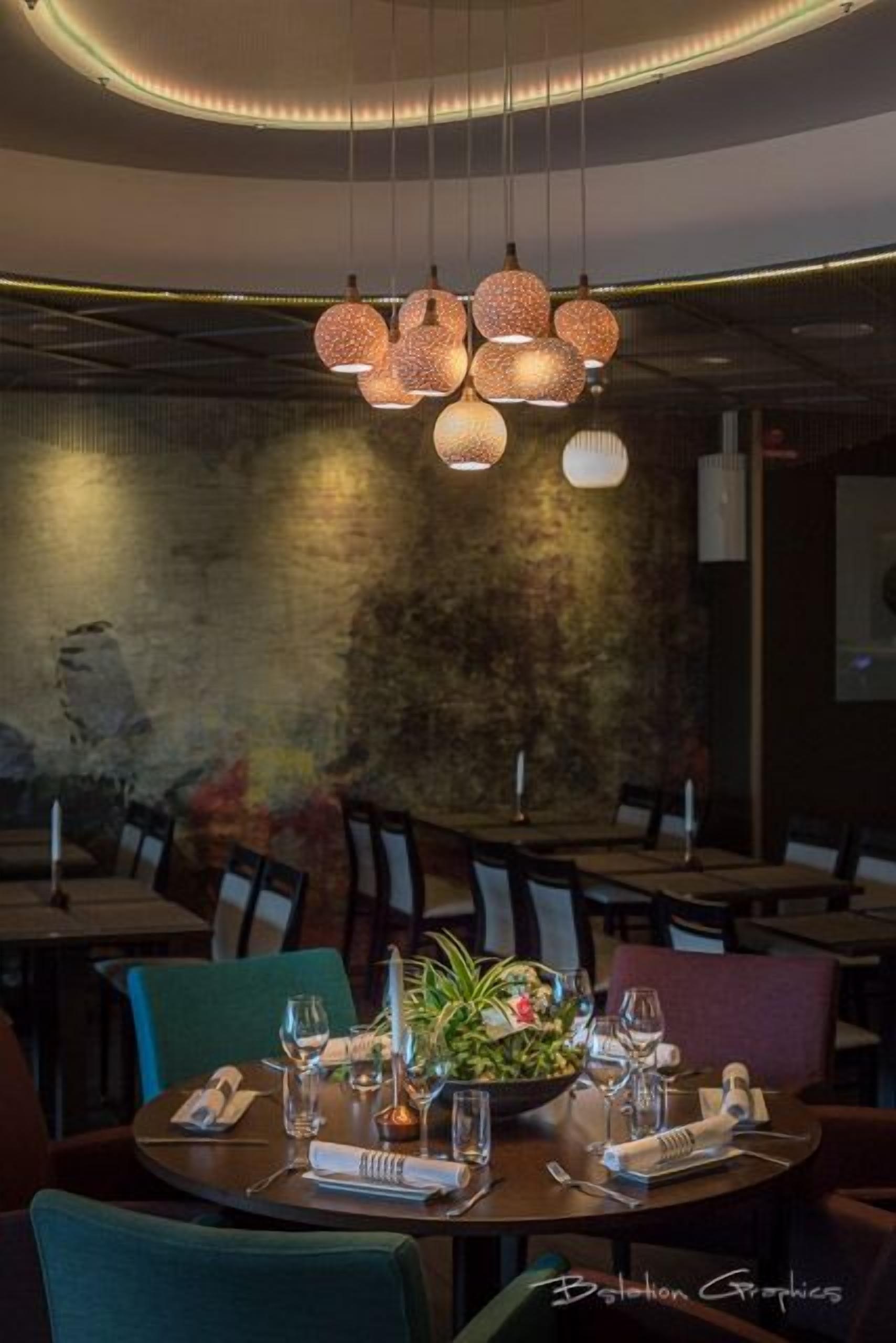 Un interior de restaurante con mesas redondas, sillas y una planta decorativa central.